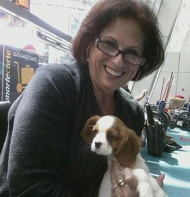 Kelly's late mother, Debbie, smiling while holding a young Blenheim Cavalier puppy